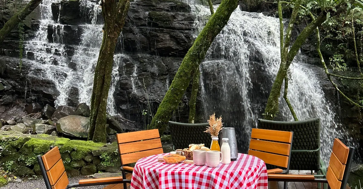 A cascata da Lumine vista do deck, com a mesa posta entre as árvores