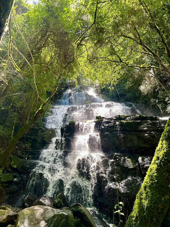 A cascata da Lumine descendo em degraus de pedra no meio da mata